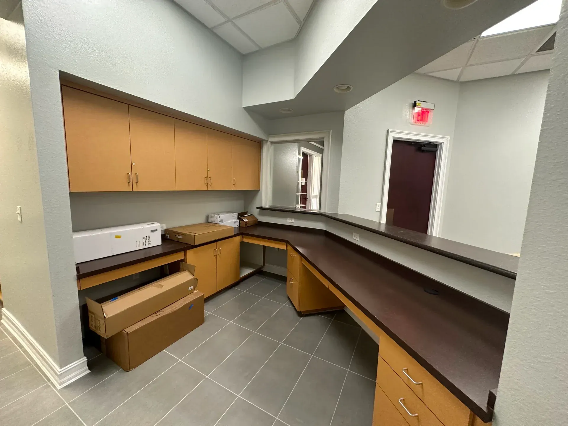 Reception area with a wraparound counter, cabinets, and a doorway. Brown and beige tones.