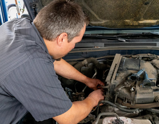 Mechanic working under an open car hood, inspecting engine components. | Lowry Repair Center Inc
