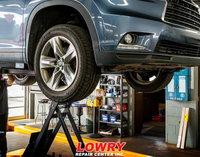 Blue SUV raised on a car lift in an auto repair shop, front wheel visible. | Lowry Repair Center Inc