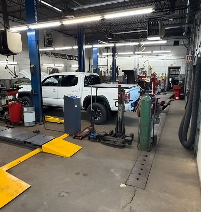 Auto repair shop with a white pickup on a lift, surrounded by tools and equipment | Lowry Repair Center Inc