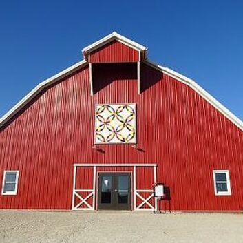 A bright red barn with a white-framed entrance and a quilt-patterned square hanging on the exterior wall.