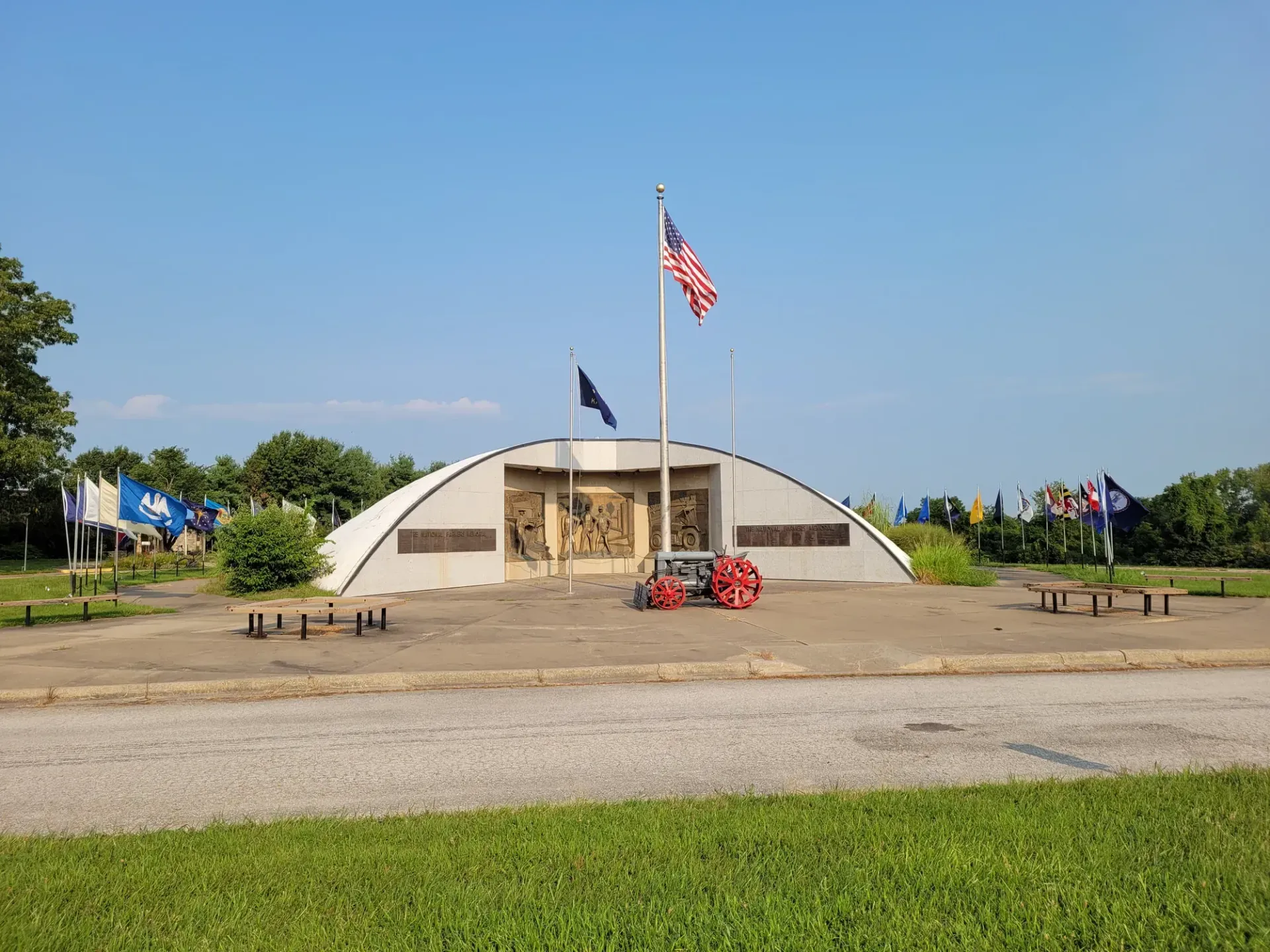A veterans memorial featuring a curved white wall, a central American flag, and surrounding flags on a grassy park area.