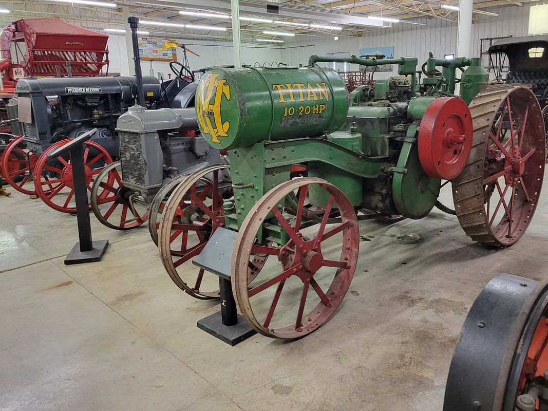 Vintage green and grey tractors with large metal wheels displayed in a well-lit indoor museum gallery.