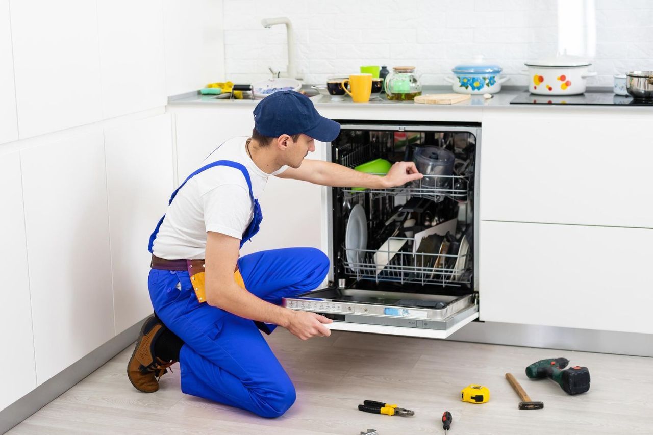 A Man Is Kneeling Down In A Kitchen Fixing A Dishwasher
