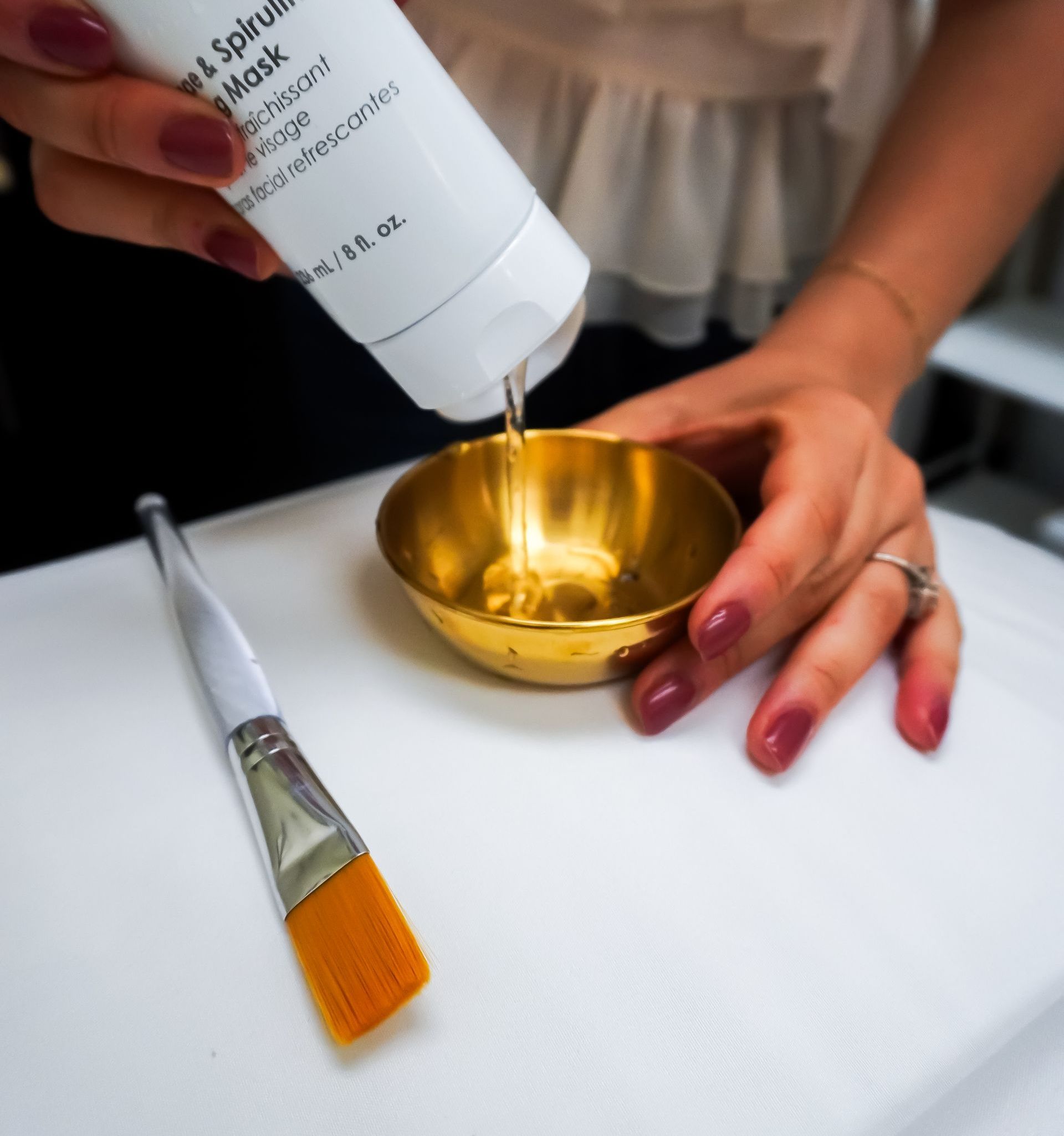 A woman is pouring a bottle of lotion into a gold bowl.