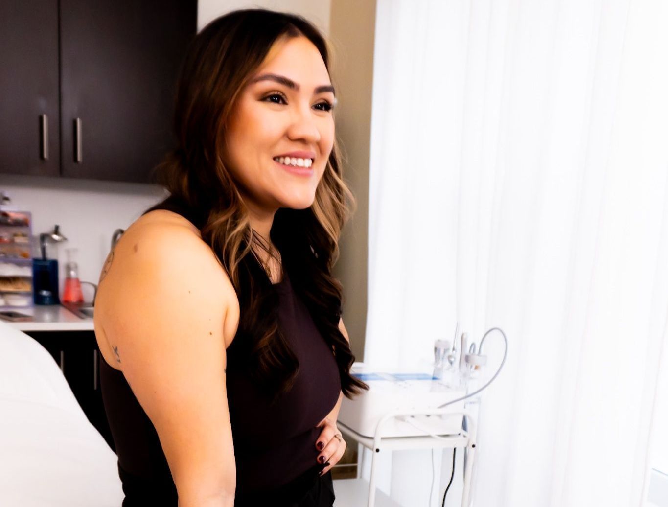 A woman is smiling while sitting in front of a window in a room.