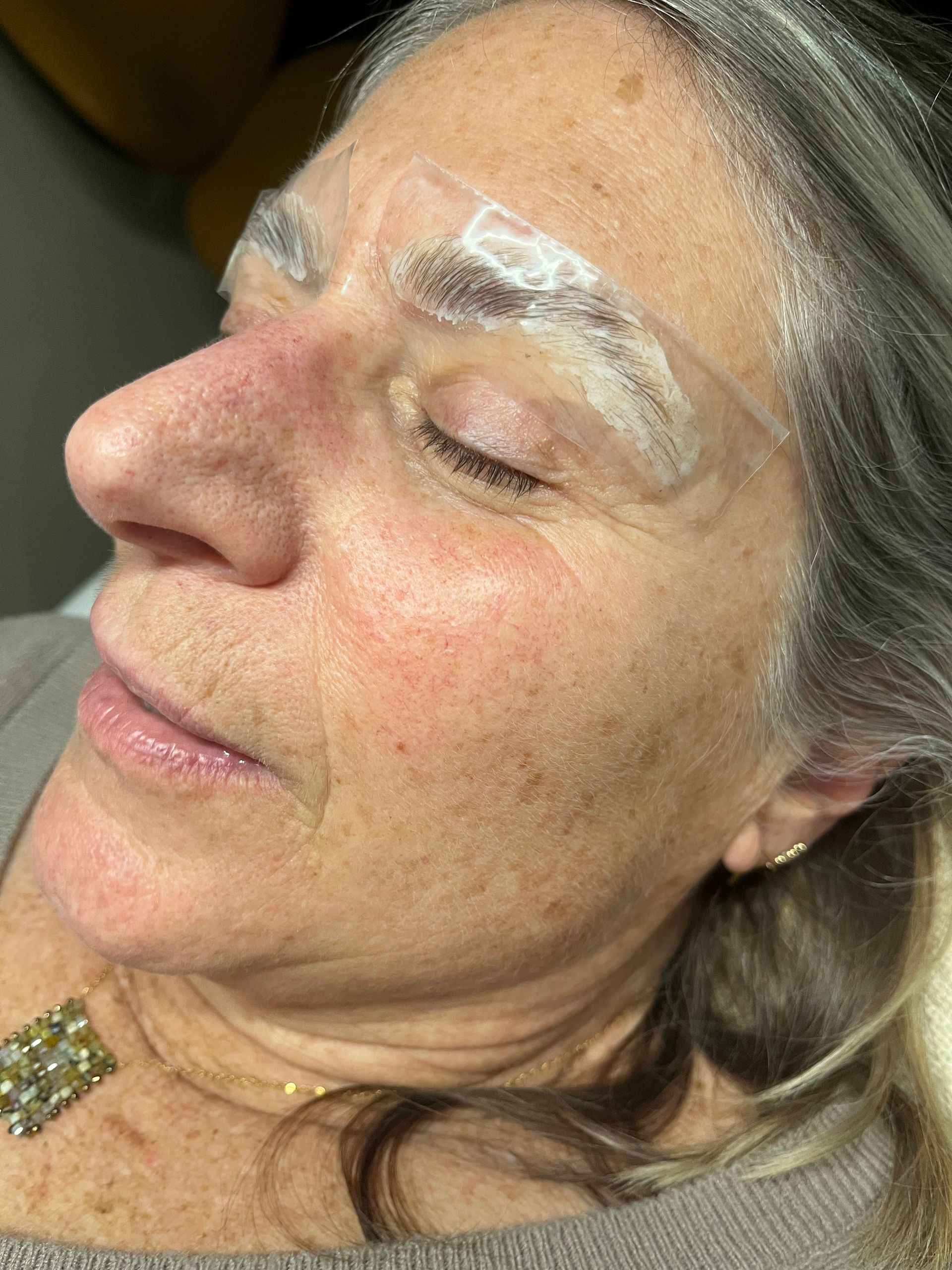 Close-up of a person's closed eye, showing brushed-up, dark eyebrows and subtle skin texture.
