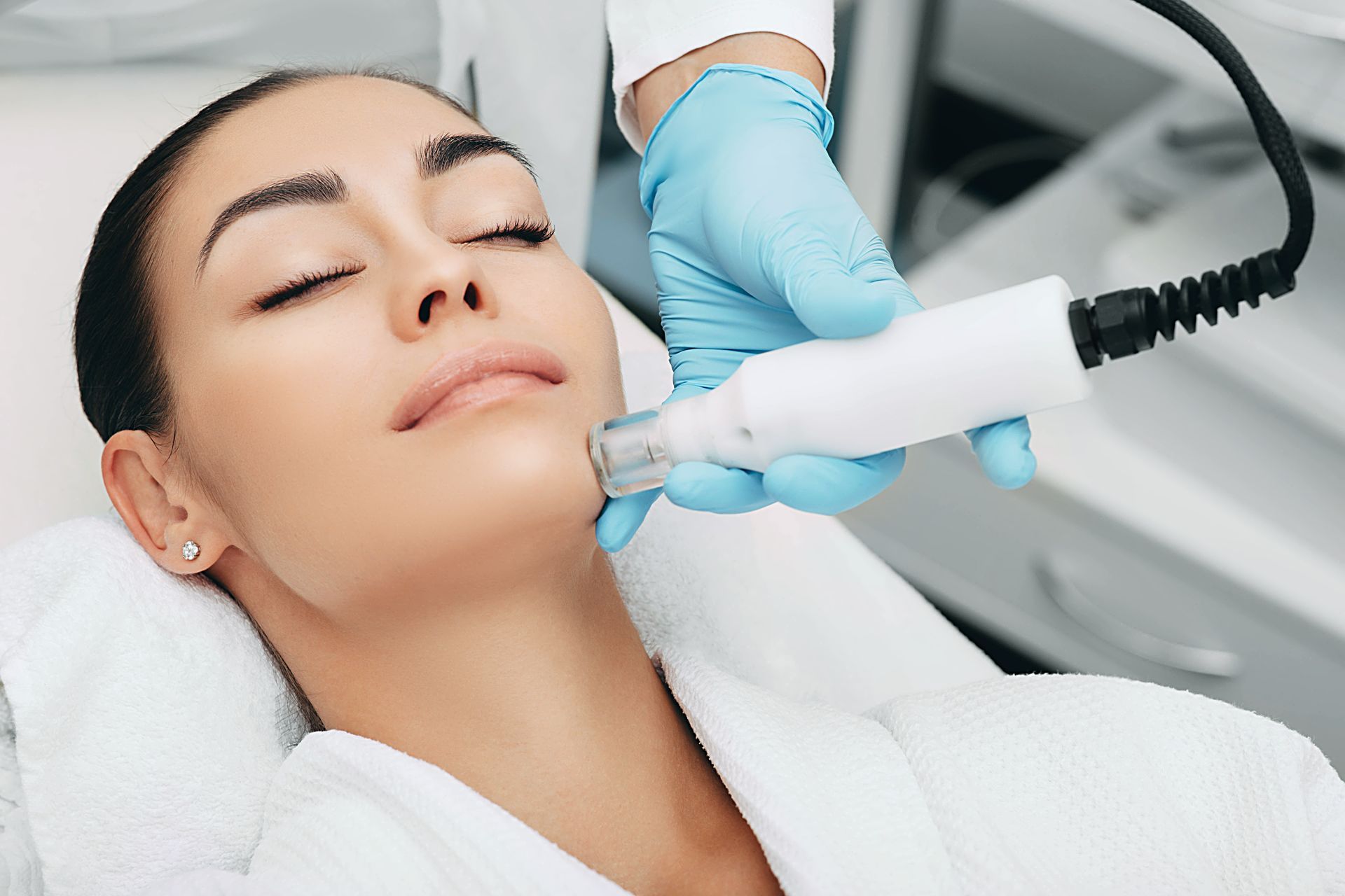 Woman receiving facial skin treatment, hand with blue glove holding device.