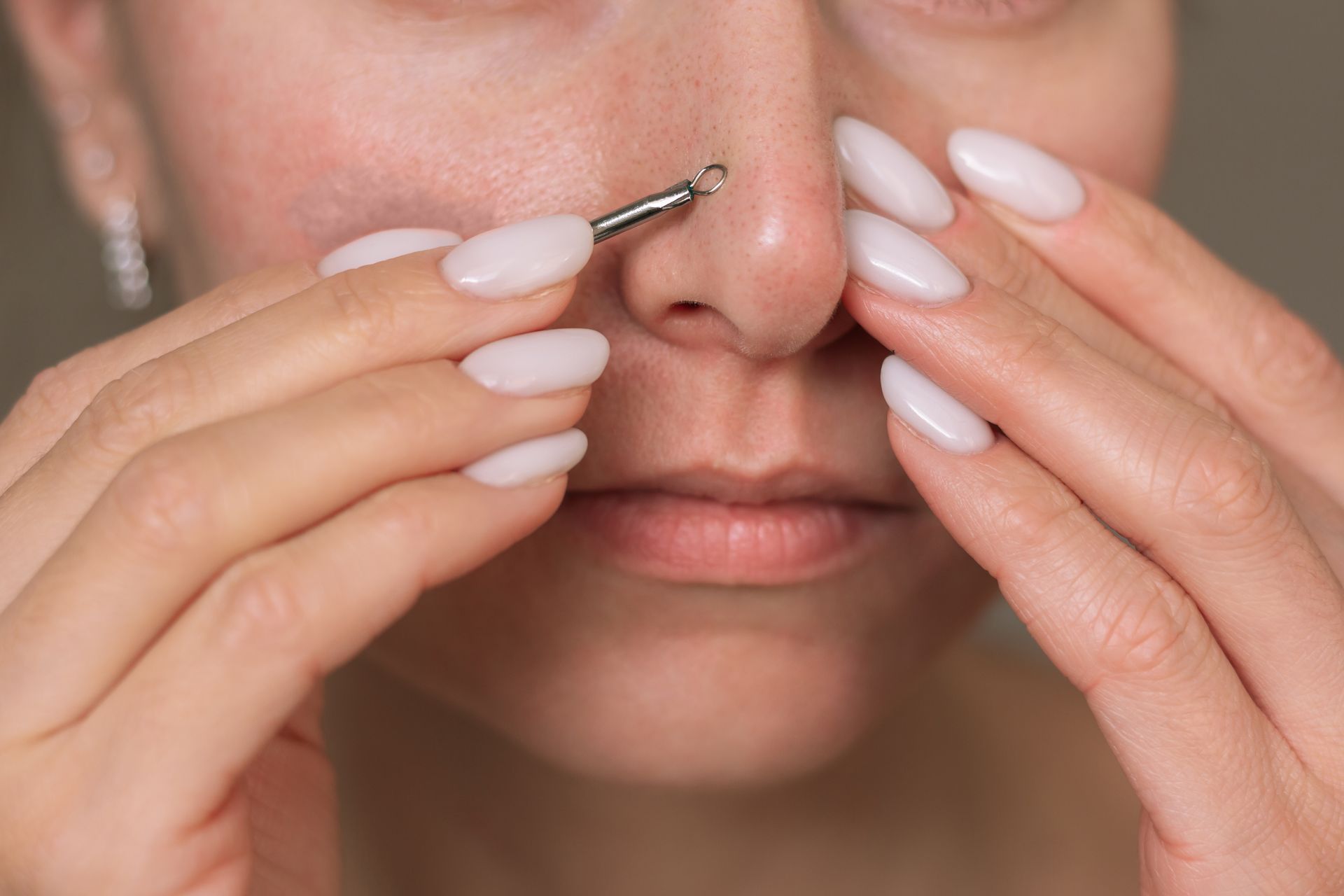 Person using a comedone extractor on their nose, holding it with both hands.
