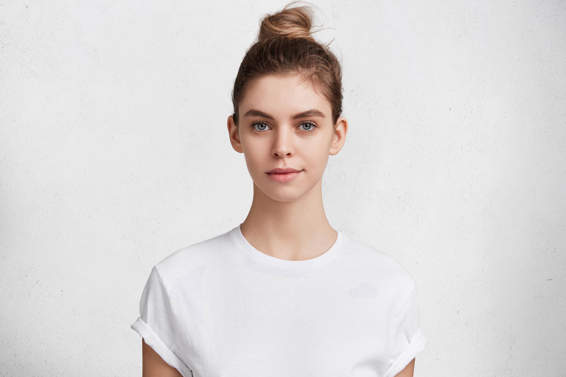 The woman is wearing a white t-shirt and has her hair in a bun.