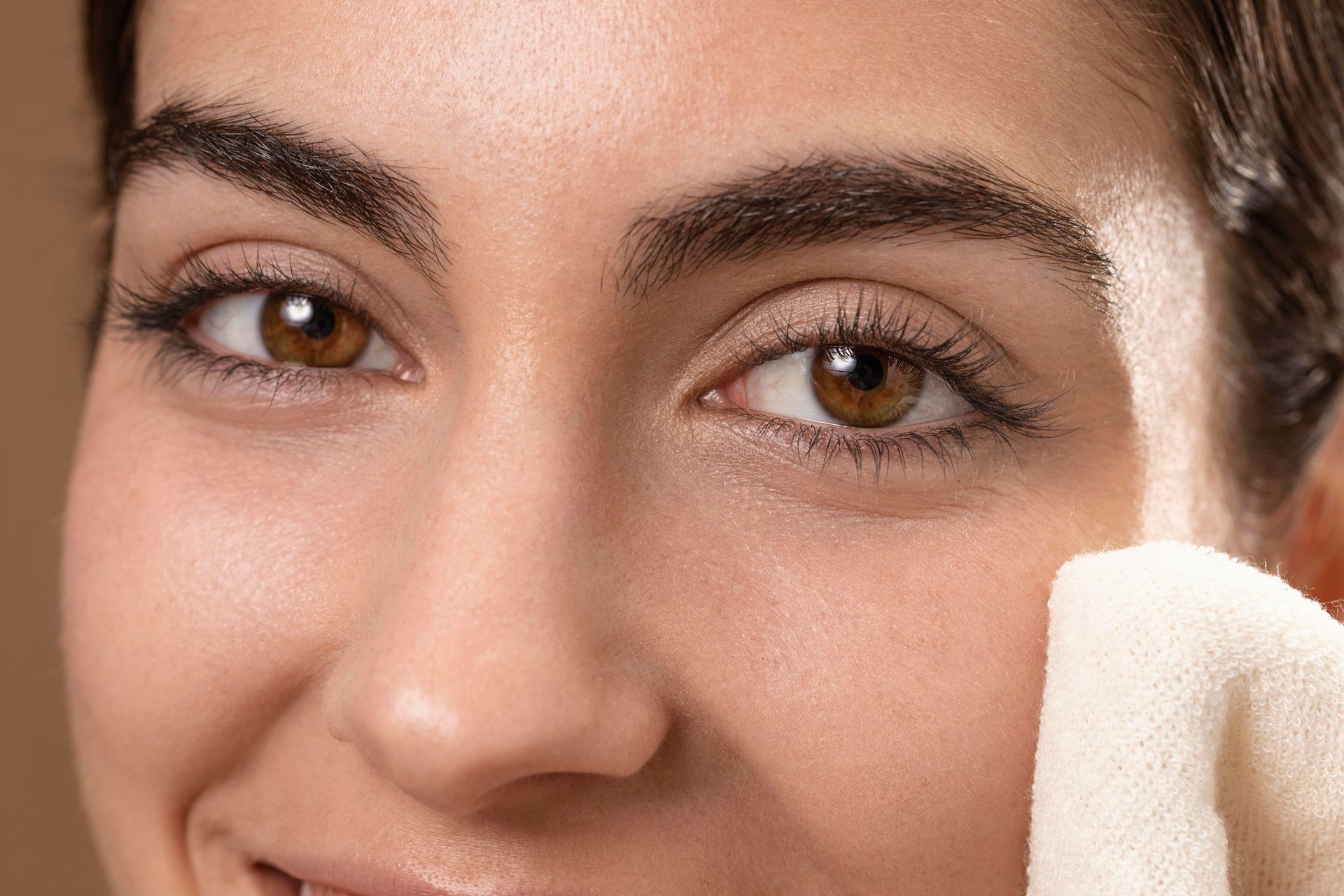 Woman wiping face with a white cloth, brown eyes, thick eyebrows, and light skin.