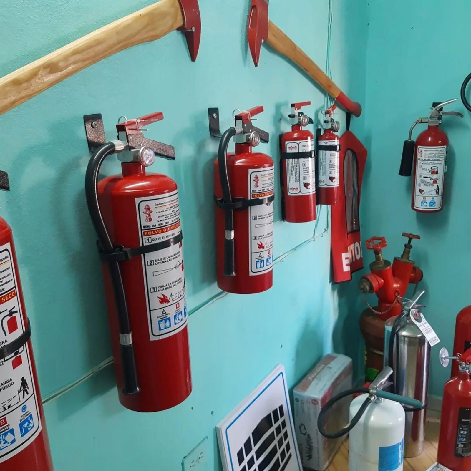 Una fila de extintores rojos están colgados en una pared.