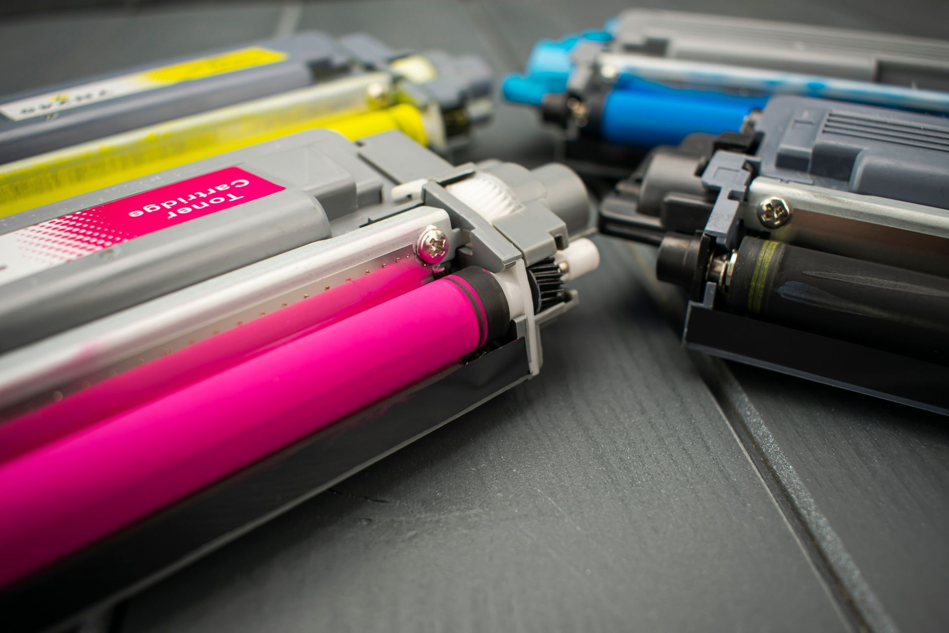 Color toner cartridges arranged on a dark surface, showing magenta, yellow, cyan, and black units