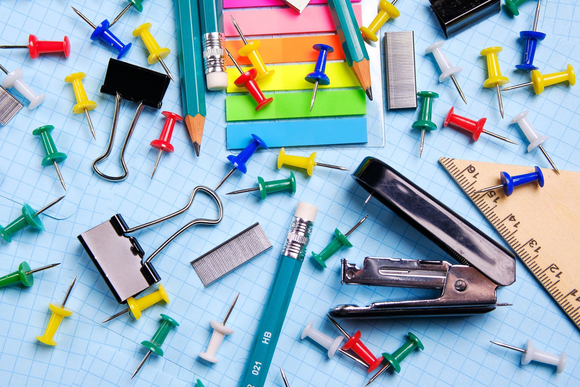 Office supplies on graph paper, including pins, pencils, clips, and stapler.
