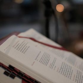 Open book with text, red ribbon bookmark, blurry background.