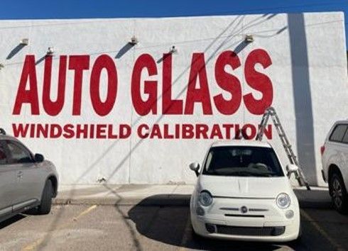 A white car is parked in front of a building that says auto glass windshield calibration — Auto Glass in Albuquerque, NM A white car is parked in front of a building that says auto glass windshield calibration