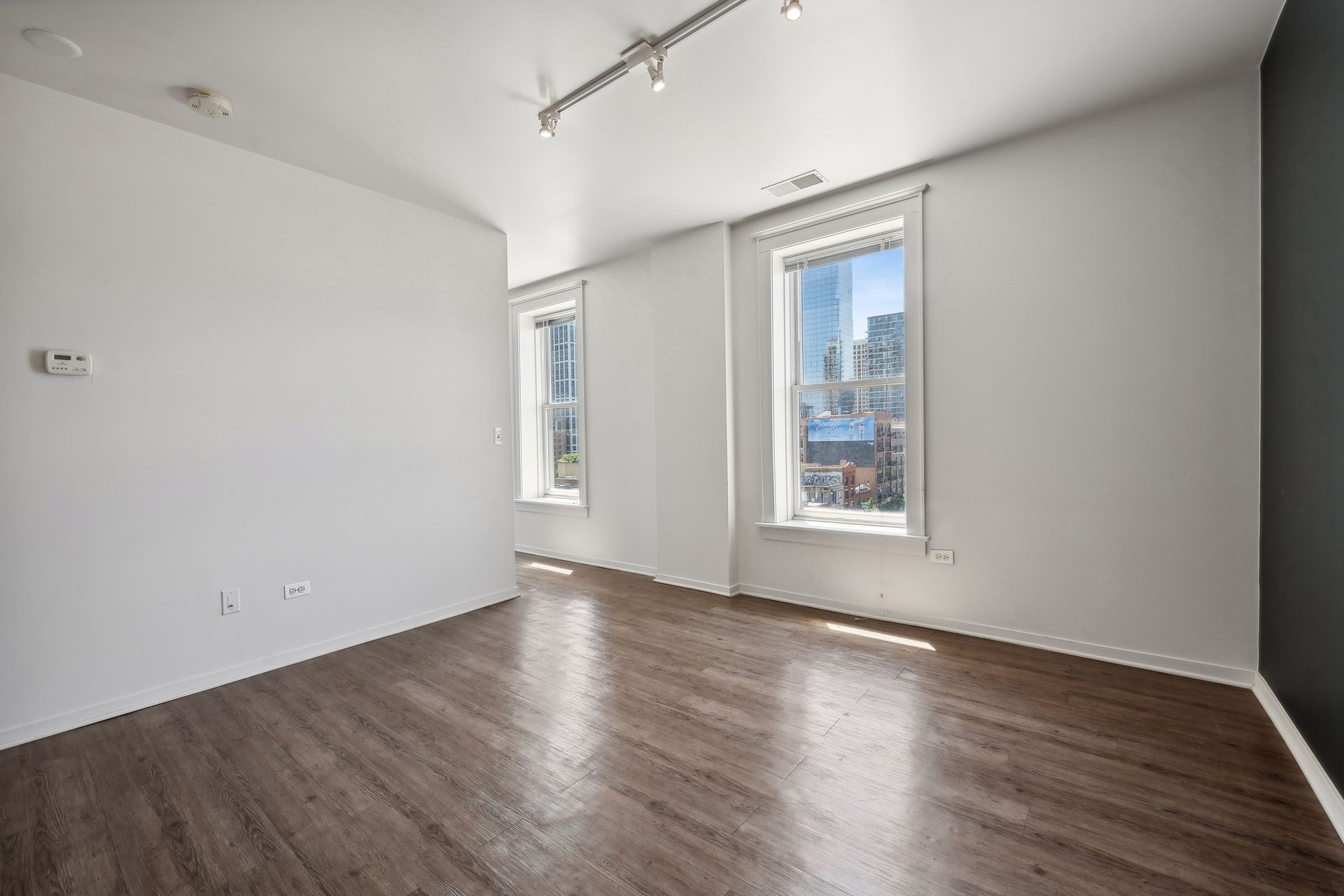 An empty living room with hardwood floors and two windows.