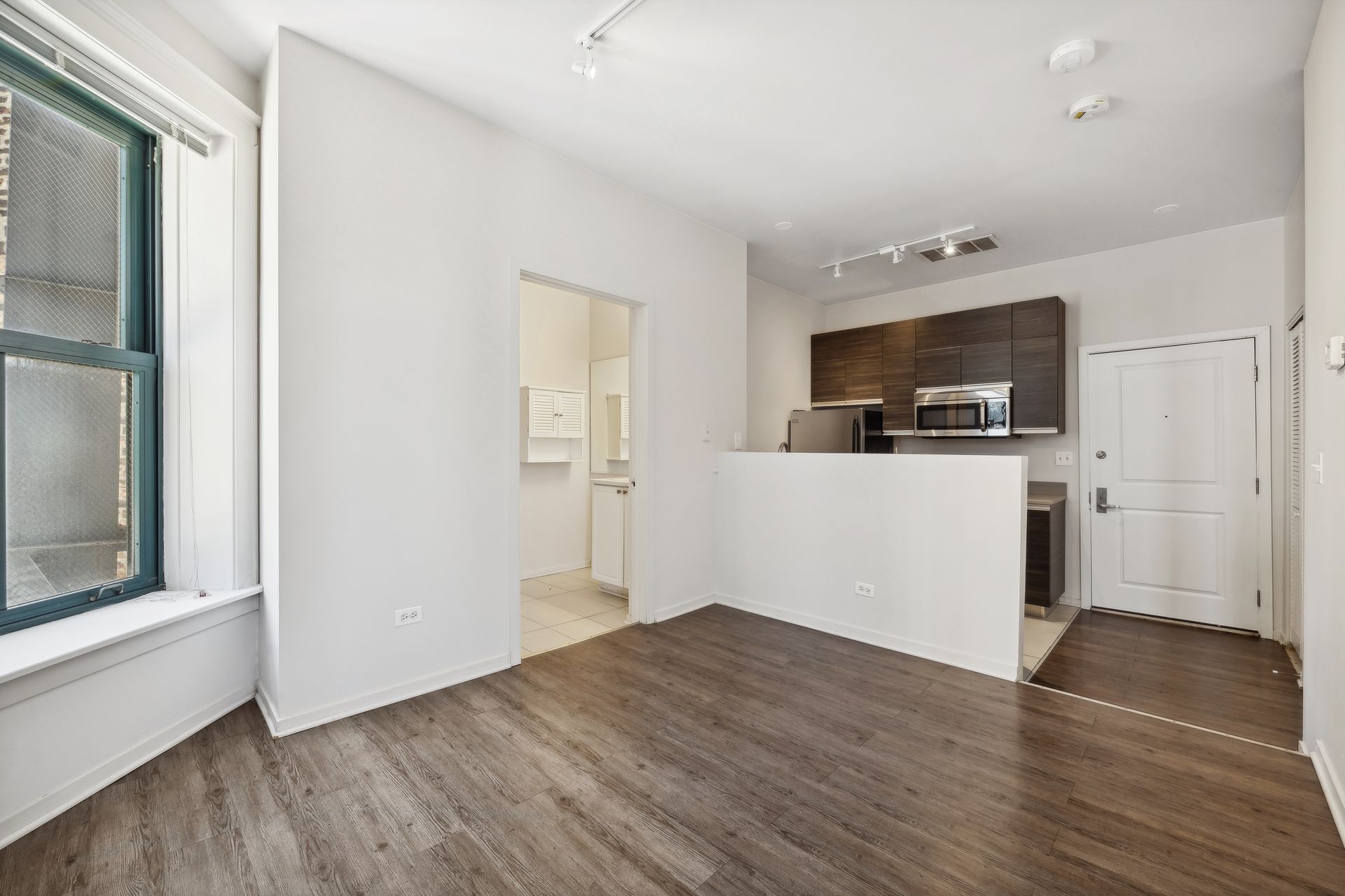 A living room with hardwood floors and a kitchen in the background.
