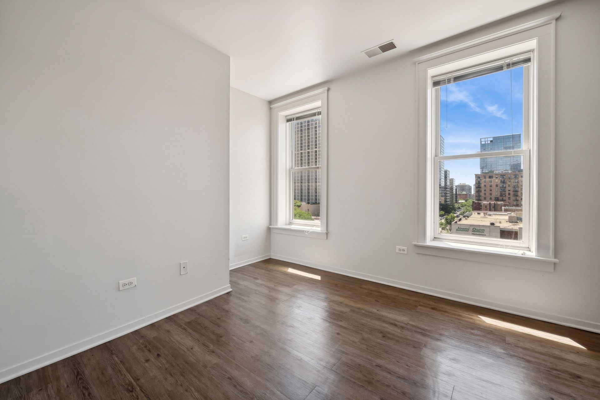 An empty room with hardwood floors and two windows.