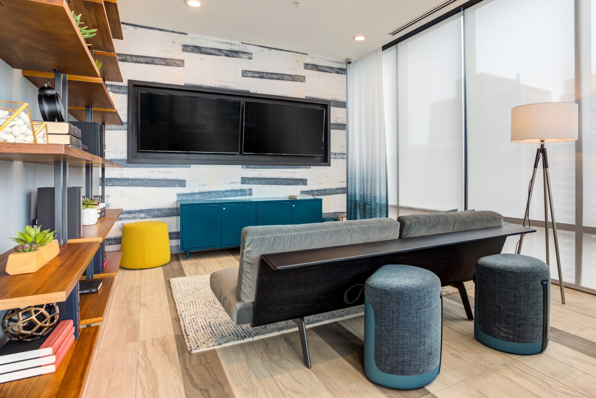 A living room with a couch , ottomans , shelves and two flat screen tvs.