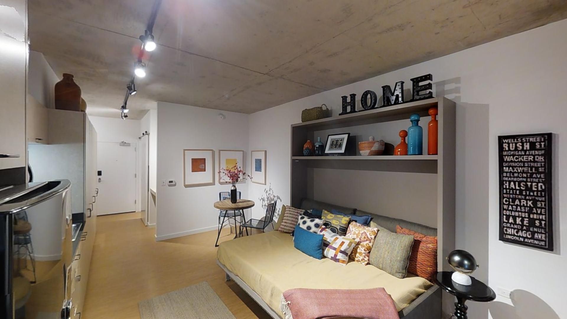 A living room with a couch and a sign that says home on the wall.
