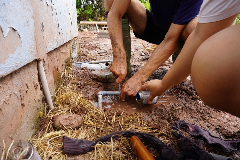People Working on Plumbing Near a Building, Hands in Mud and Water — Full On Plumbing & Gas in Winnellie, NT
