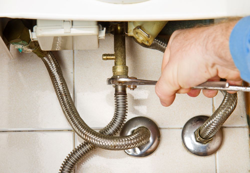 Person Using a Wrench to Tighten Plumbing Fixtures Under a White Cabinet — Full On Plumbing & Gas in Winnellie, NT