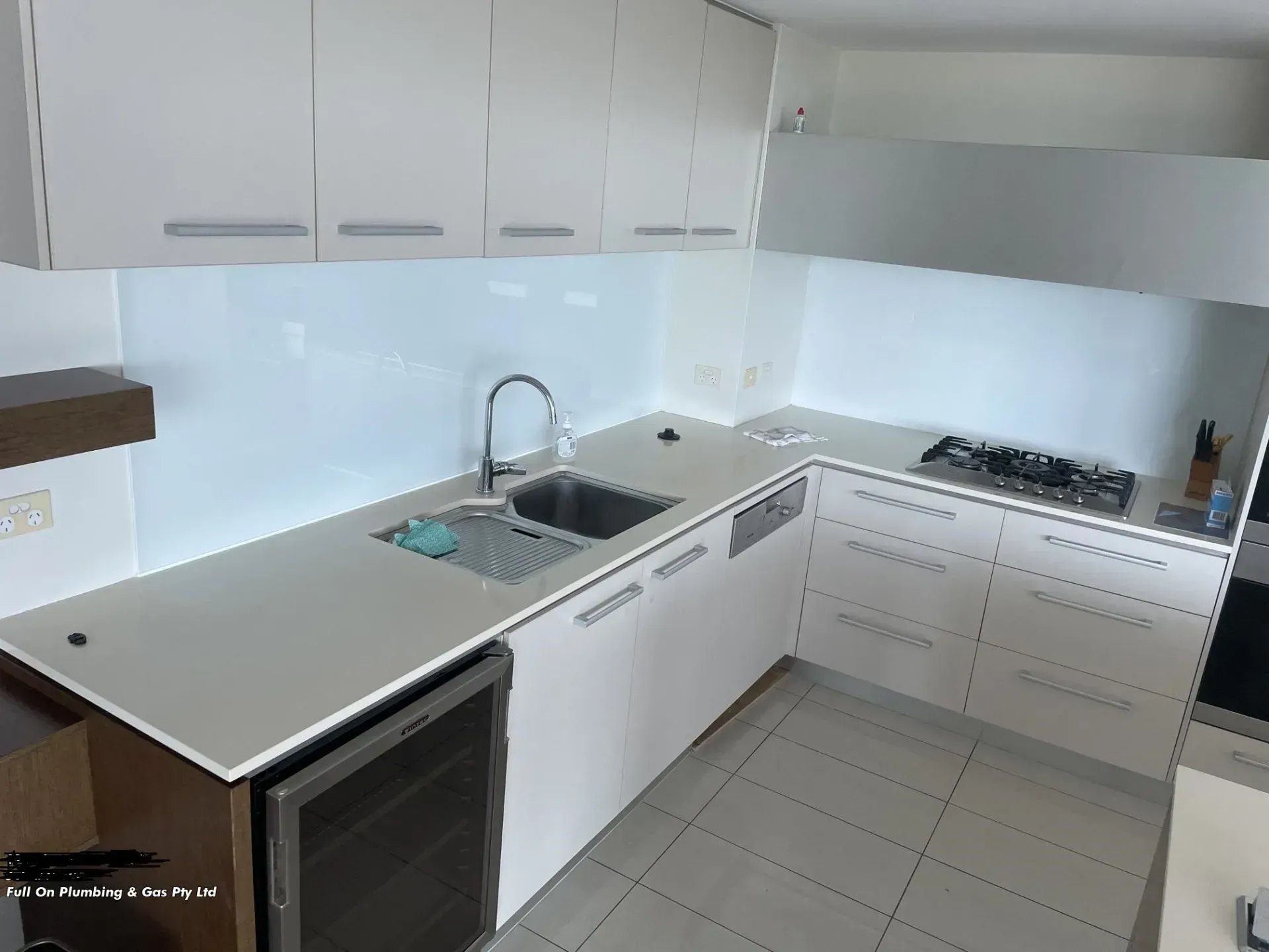 White Modern Kitchen With Overhead Cabinets, Sink, and Stovetop — Full On Plumbing & Gas in Winnellie, NT