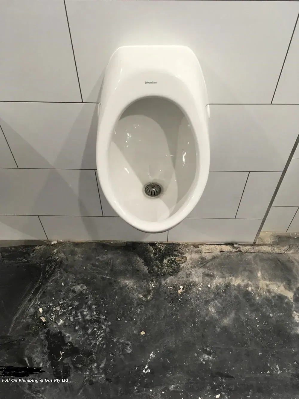White Urinal Mounted on a Tiled Wall Above a Dark, Stained Floor — Full On Plumbing & Gas in Winnellie, NT