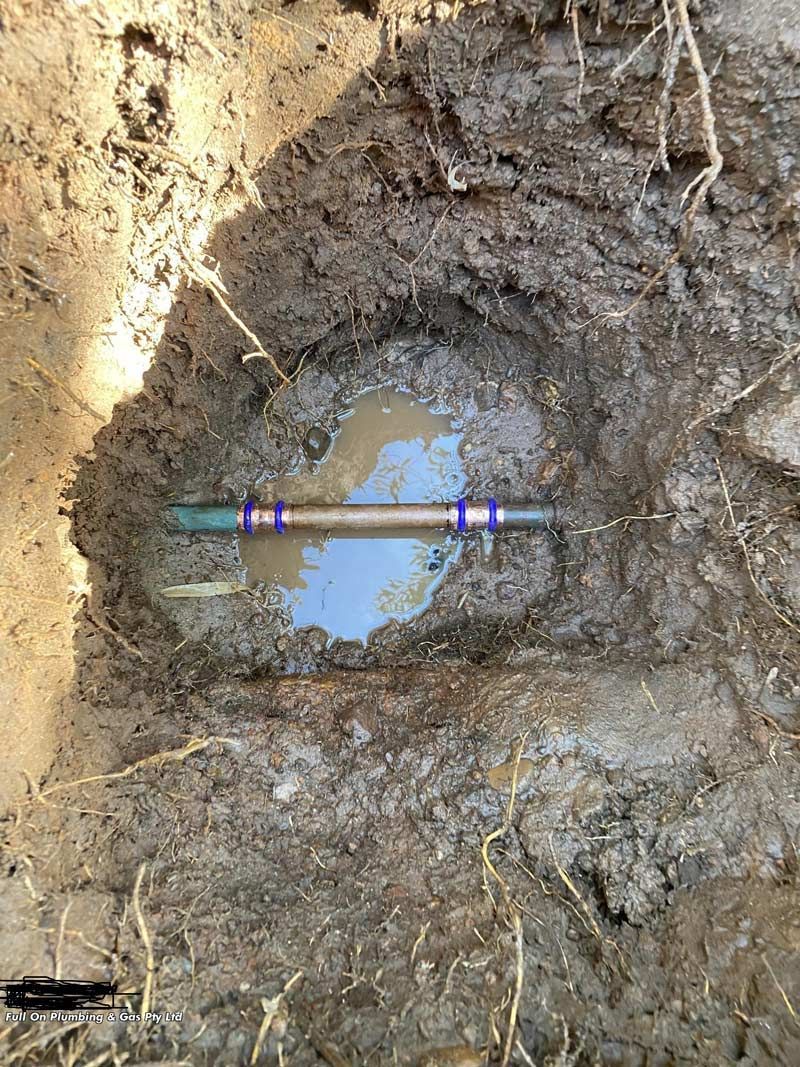 A Hole in the Ground Filled With Muddy Water, Revealing a Pipe With Blue Rings — Full On Plumbing & Gas in Winnellie, NT