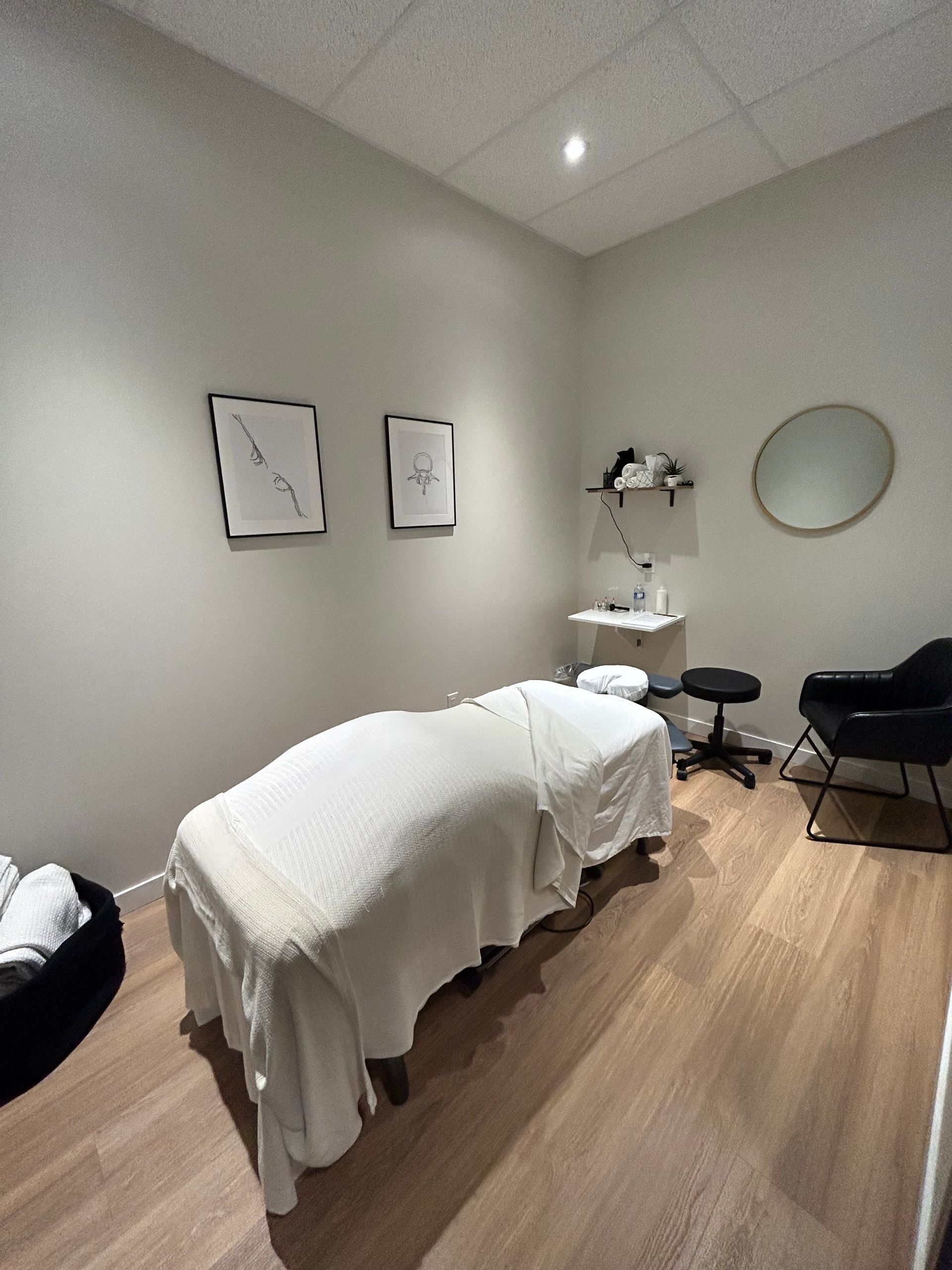 massage table with a chair in the corner and a framed picture above, mirror on the right