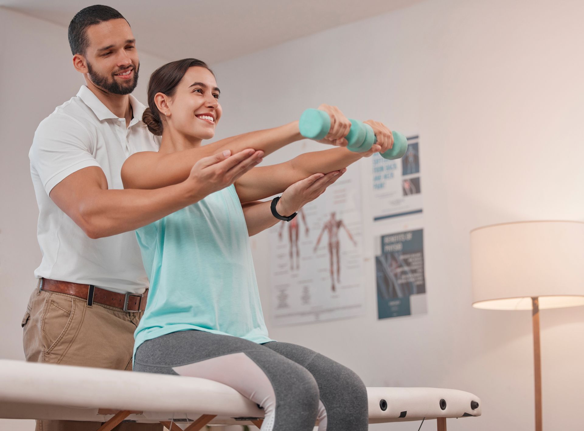 A man is helping a woman lift a dumbbell while sitting on a table.