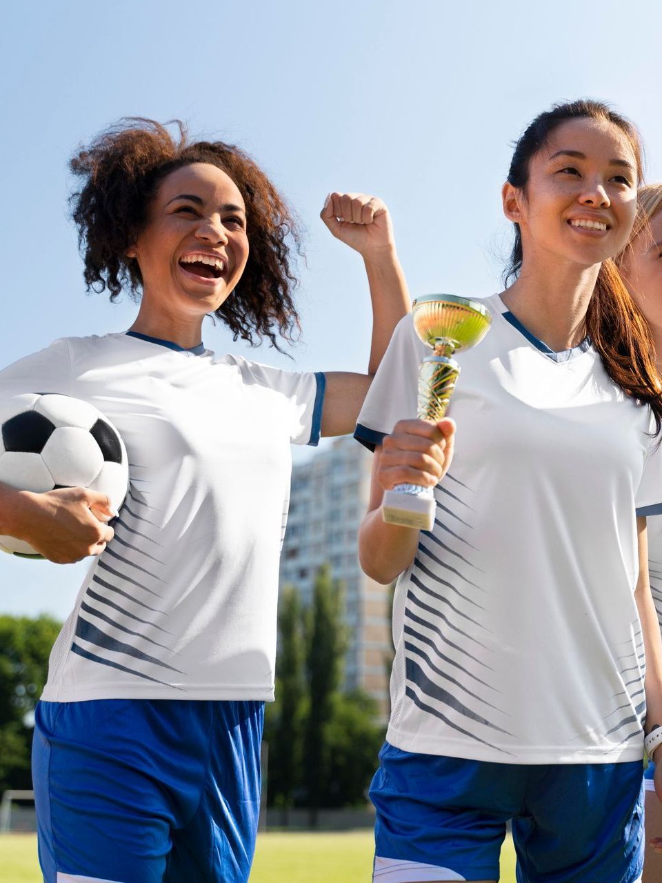 Three female soccer players are holding a trophy and a soccer ball.