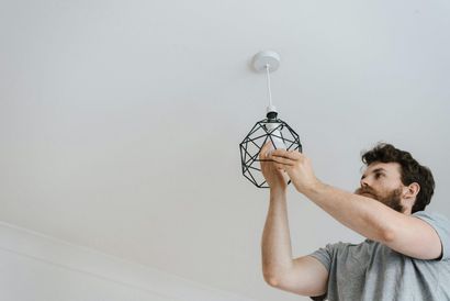 Man installing a black geometric ceiling light fixture on a white ceiling