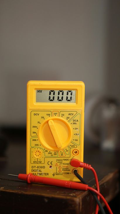 Yellow digital multimeter on a table showing 0.00, with red and black probes attached