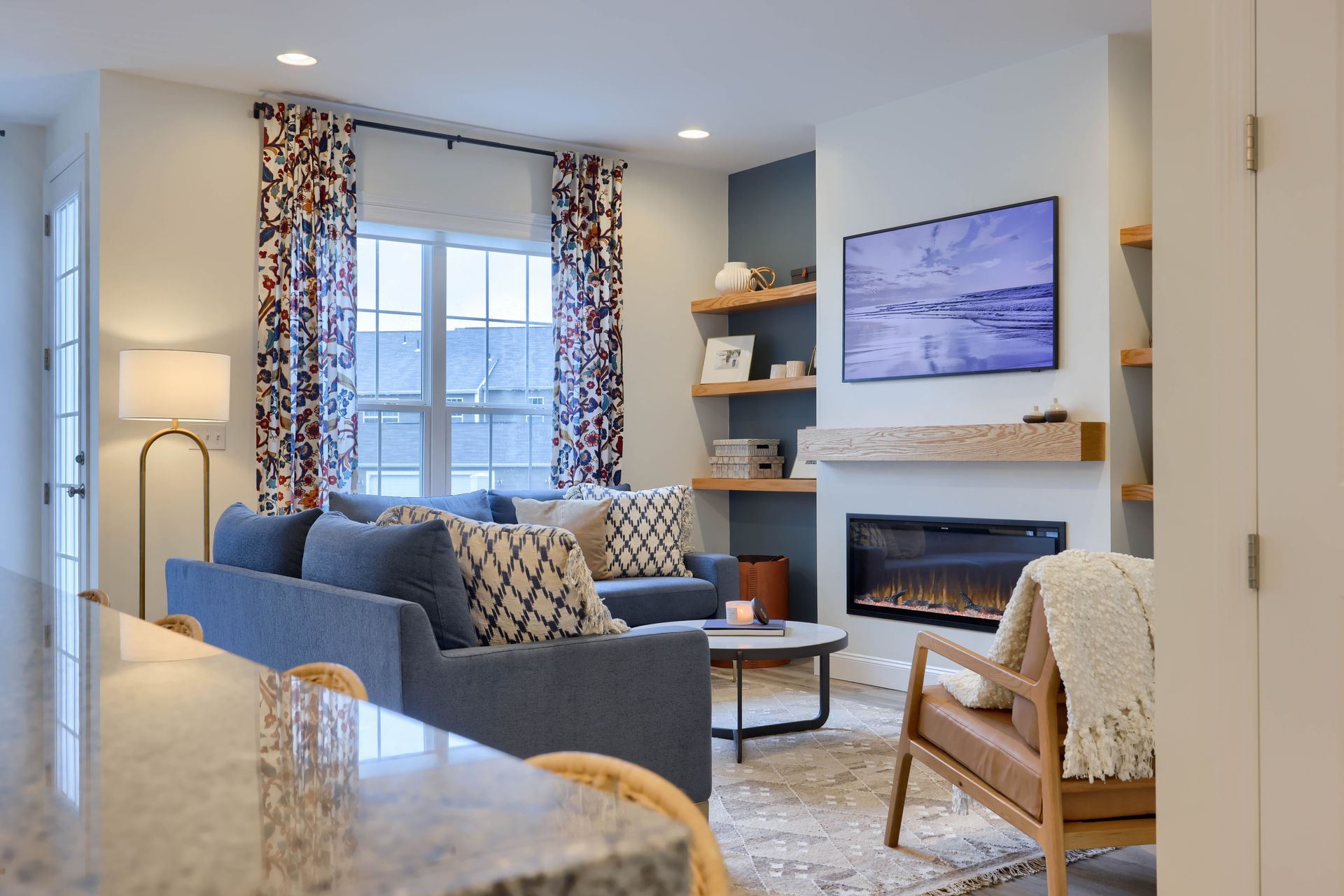 Living room with blue sofa, modern fireplace, floating shelves, and statement curtains