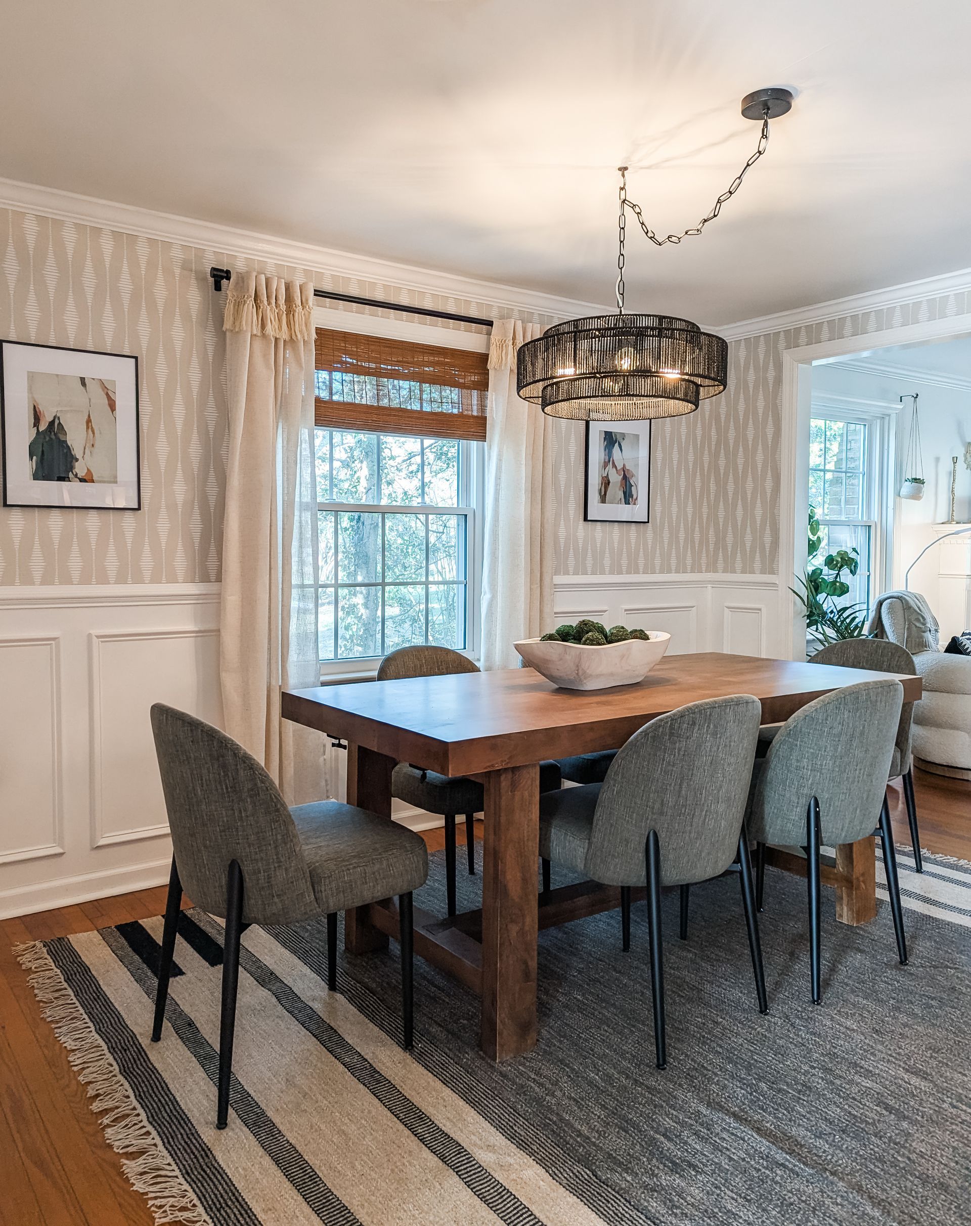Neutral dining room with warm wood dining table, black rattan chandelier, and geometric wallpaper