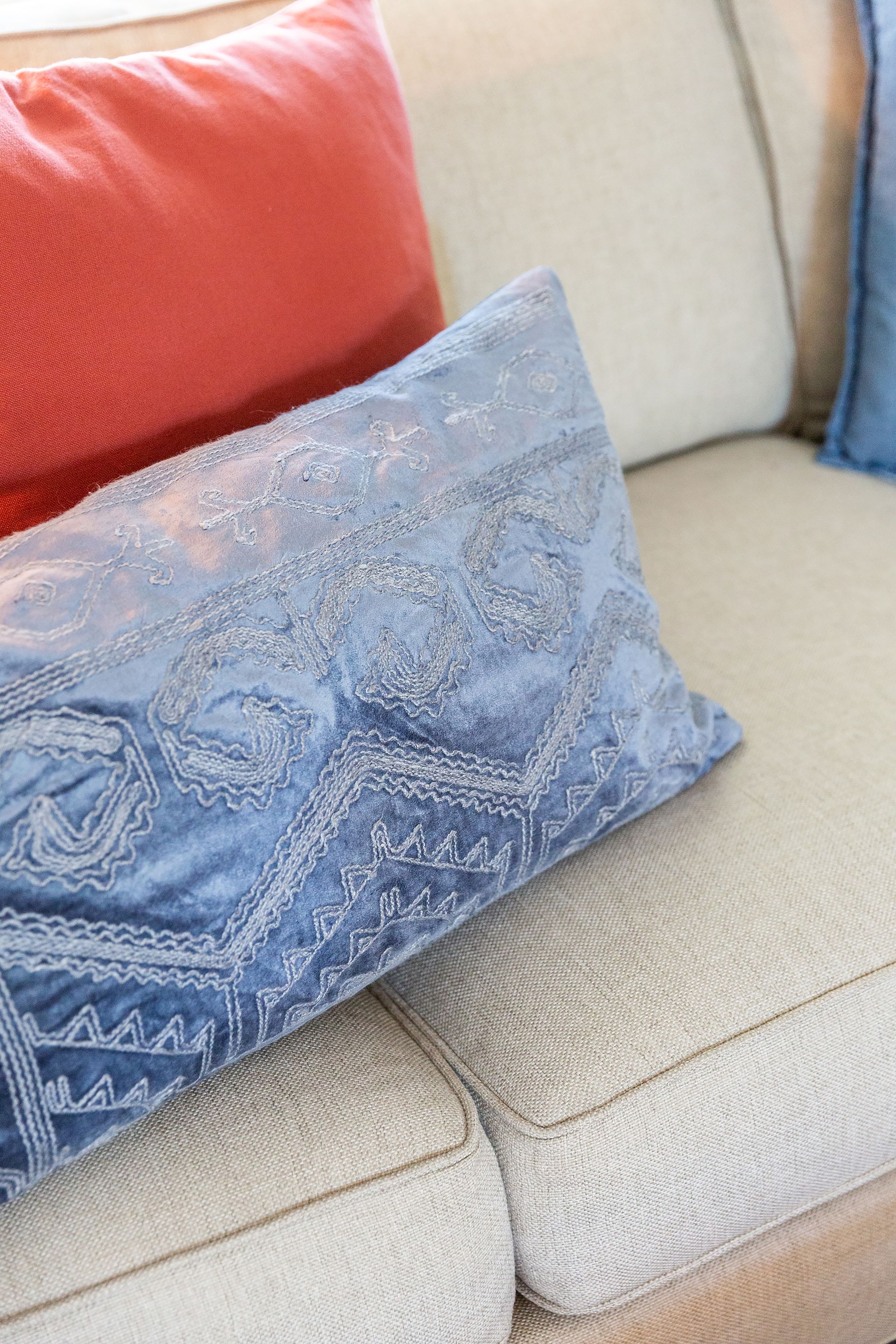 A blue pillow is sitting on a white couch next to a red pillow.