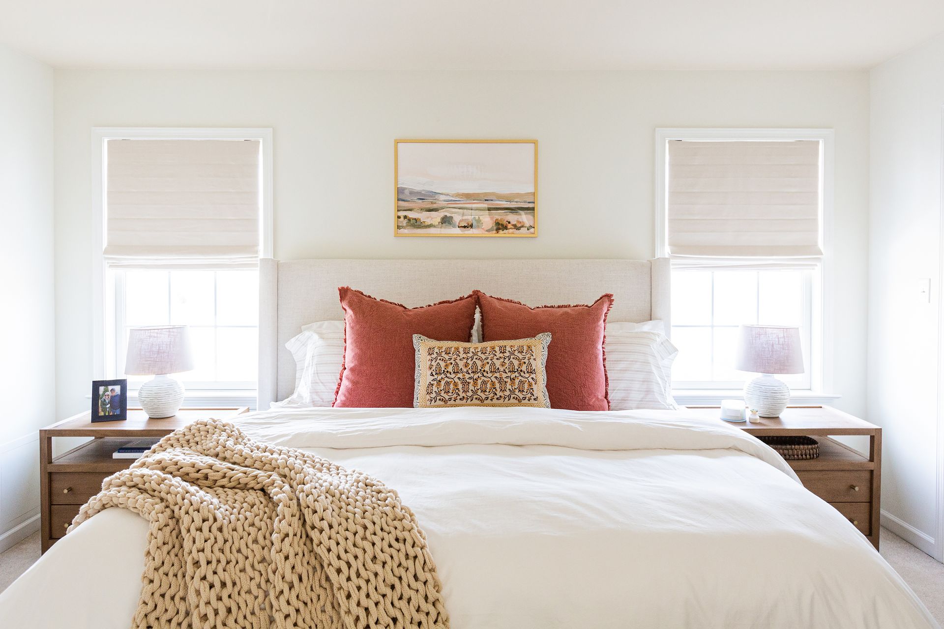 A primary bedroom with cream bedding and headboard, terracotta pillows, and chunky throw blanket