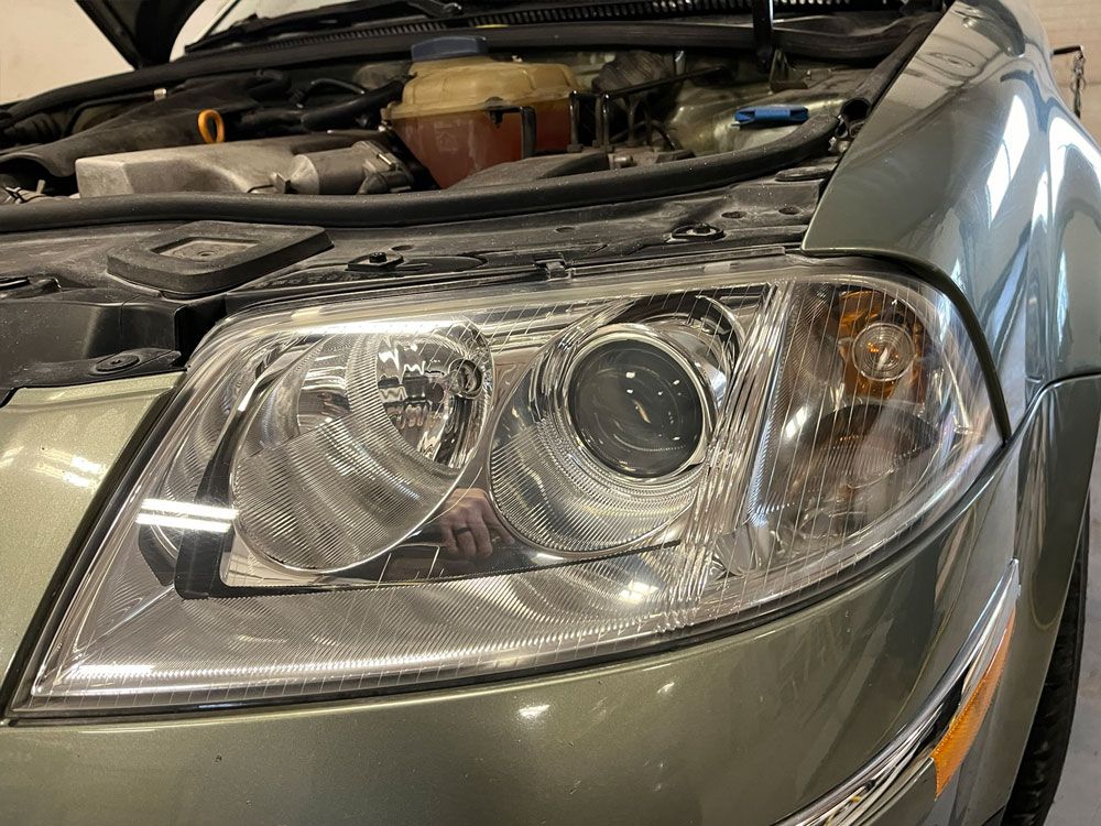 Close-up of a silver car’s front headlight with the hood open