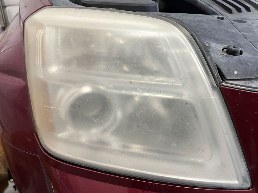 Close-up of a foggy, cloudy car headlight on a red vehicle.