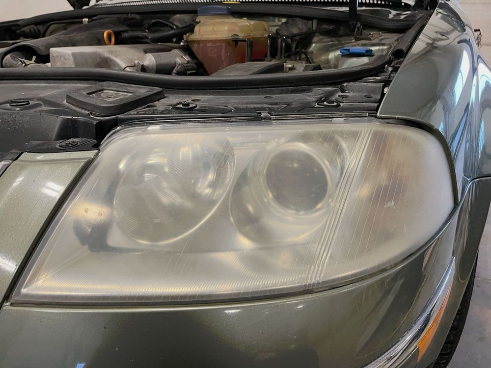 Close-up of a car's cloudy headlight with the hood open.