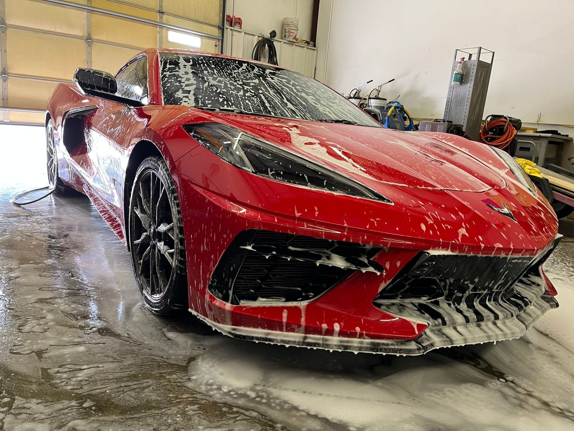 Red sports car being washed in a garage, covered in soap and water splashes