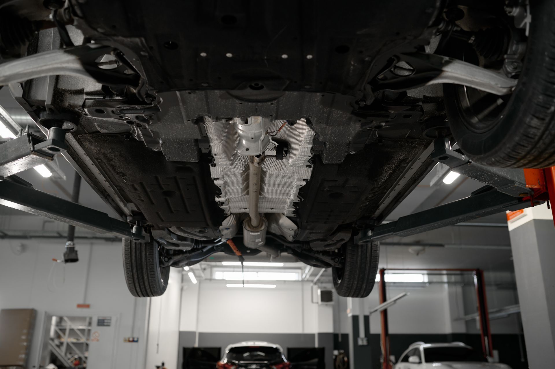 Underneath view of a car on a lift in a garage, showing the chassis and exhaust system