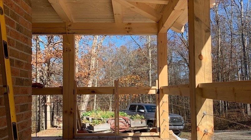 Wooden porch frame under construction, brick wall on left, view of trees and truck in background.