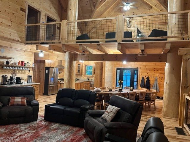 Wooden cabin interior with loft, couches, dining table, kitchen, and antler decor.