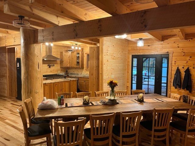 Large wooden dining table with chairs, open kitchen, and black doors in a log cabin style dining room.