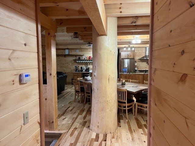Interior view of a wooden cabin, showing a kitchen with a natural log pillar and a dining table.