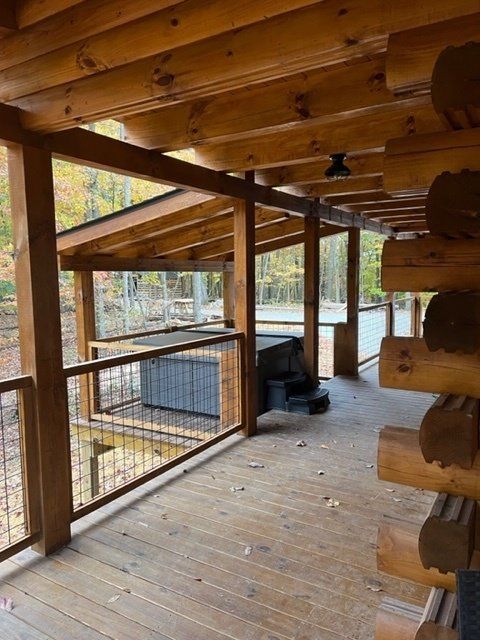 Covered wooden deck with a hot tub and log cabin exterior.