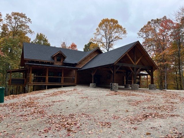 Cabin-style building with a covered porch and driveway, set in a forest with autumn foliage.